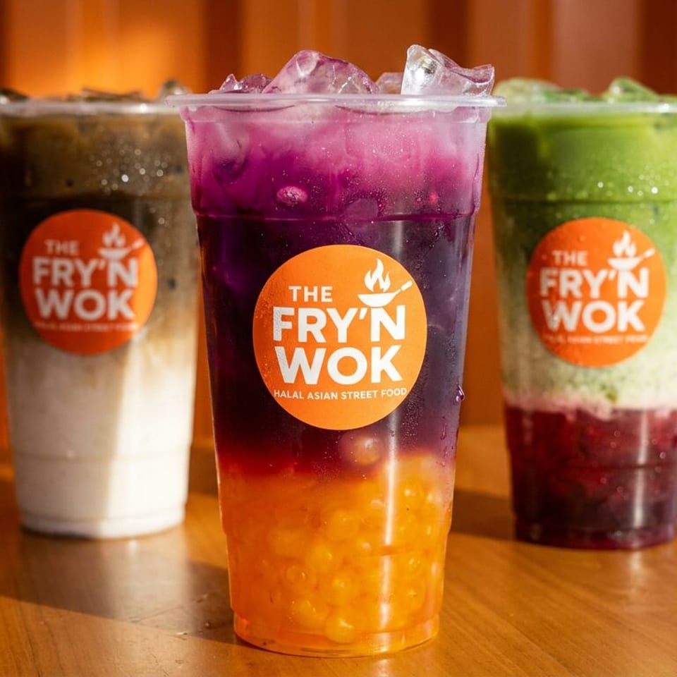 Three colorful layered drinks from The Fry'n Wok, with logos, on a wooden table.